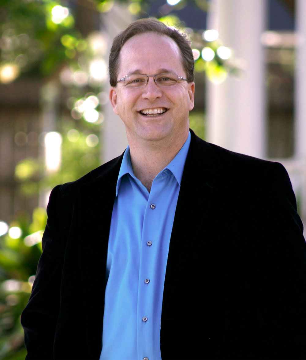 Middle aged male with light skin wearing glasses and smiling